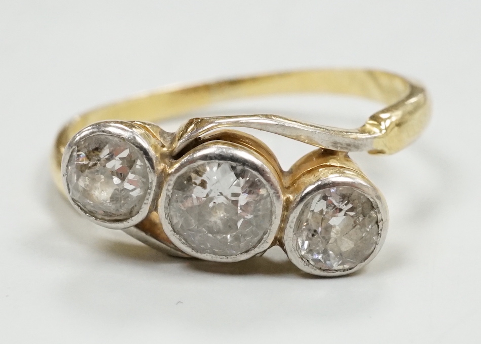 A yellow metal and collet set three stone diamond crossover ring, size N/O, gross weight 3 grams.